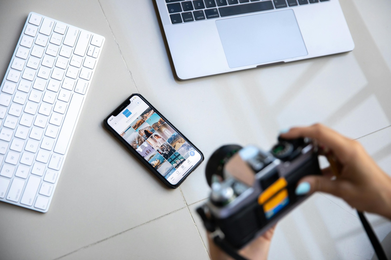 A woman holds a camera for social media photos, with a phone and laptop on the floor.