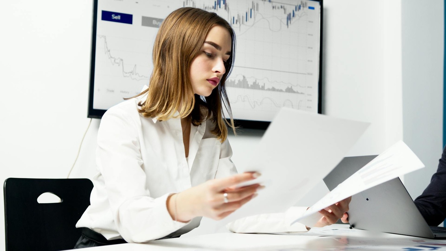 A woman in white dress shirt holding pieces of paper.