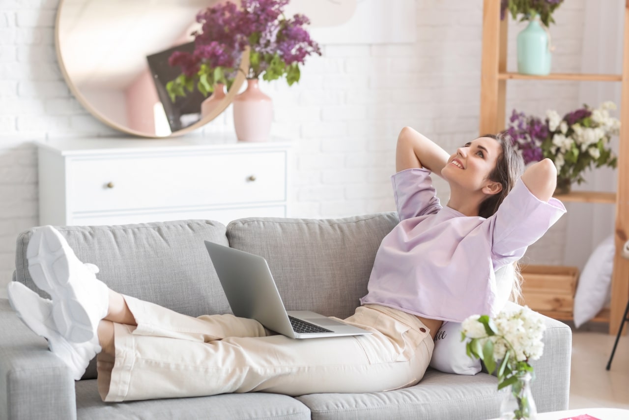 A young woman relaxes at home with a laptop on her lap, comfortably selling products online.