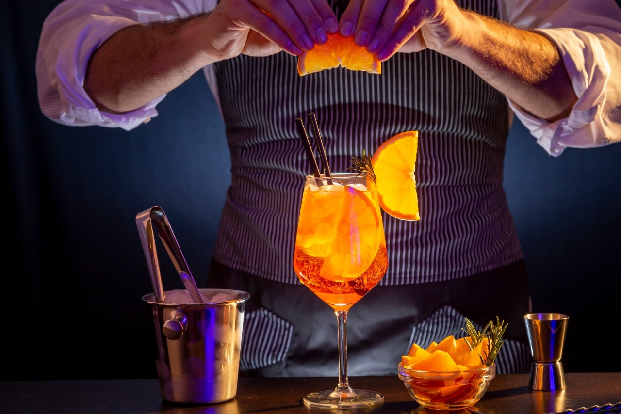 Bartender decorating Aperol spritz cocktail, adding a slice of orange.