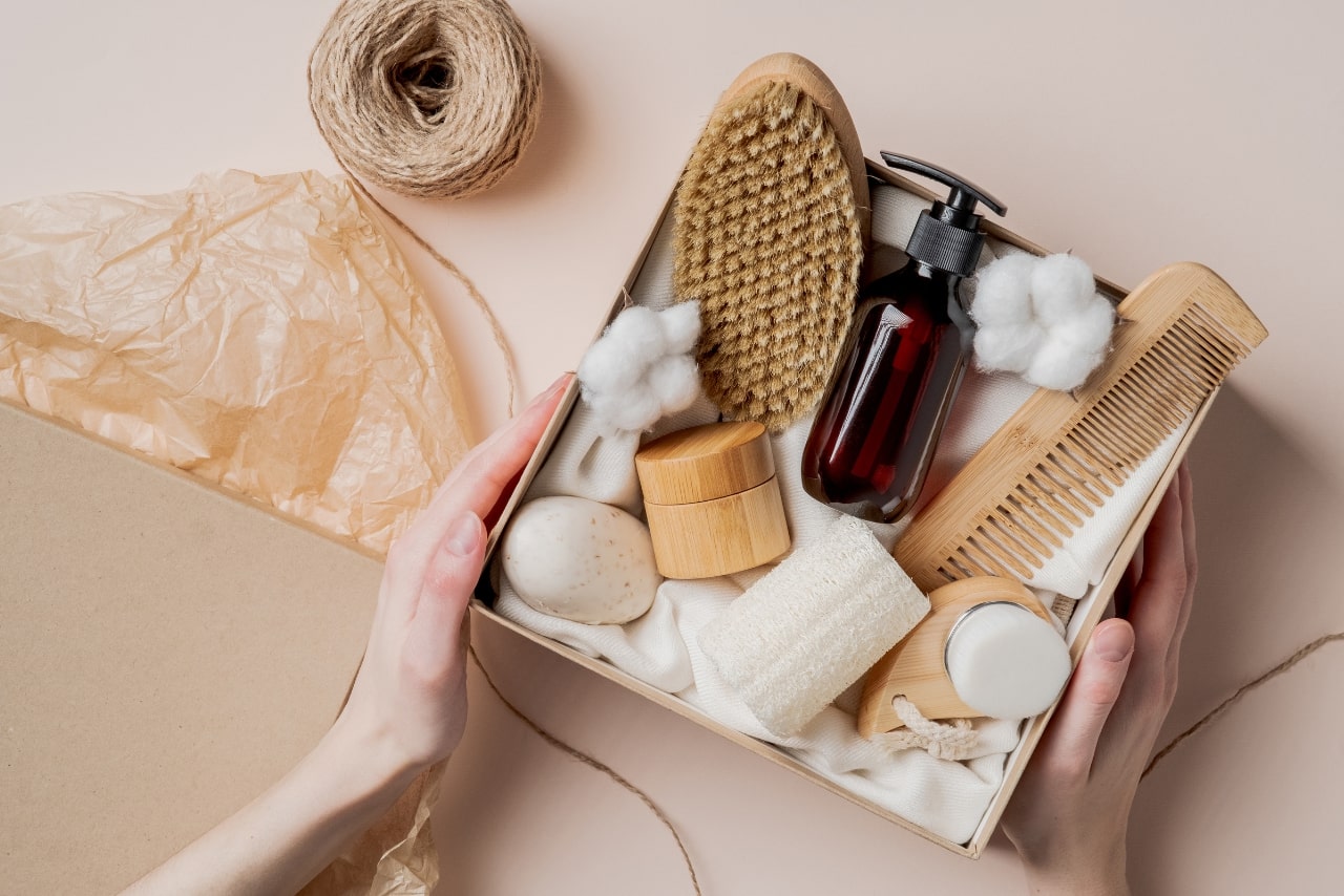 Female hands holding gift box with natural skincare products, body brush, shampoo and soap.
