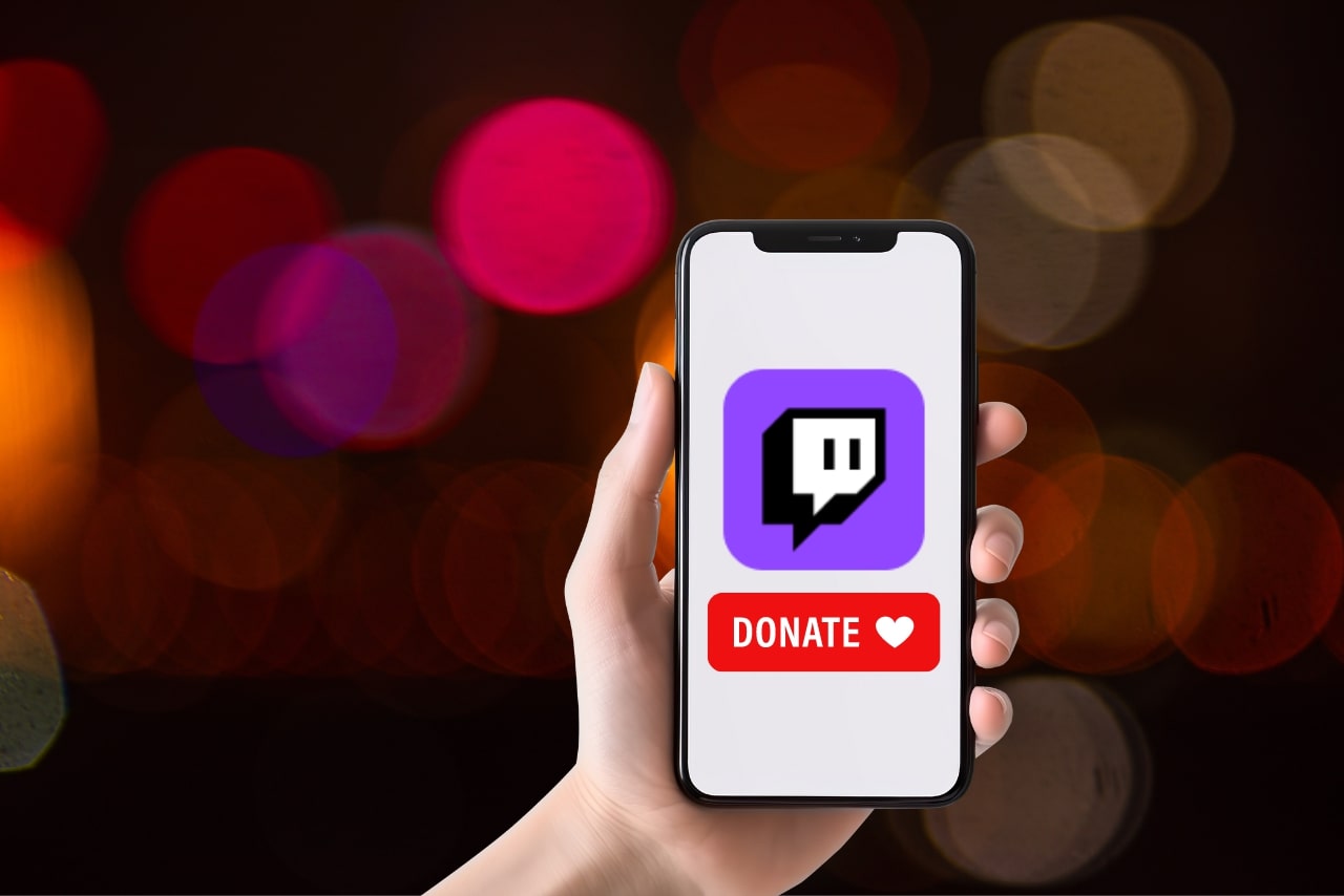 Hand holding phone while screen shows twitch logo and donate button.