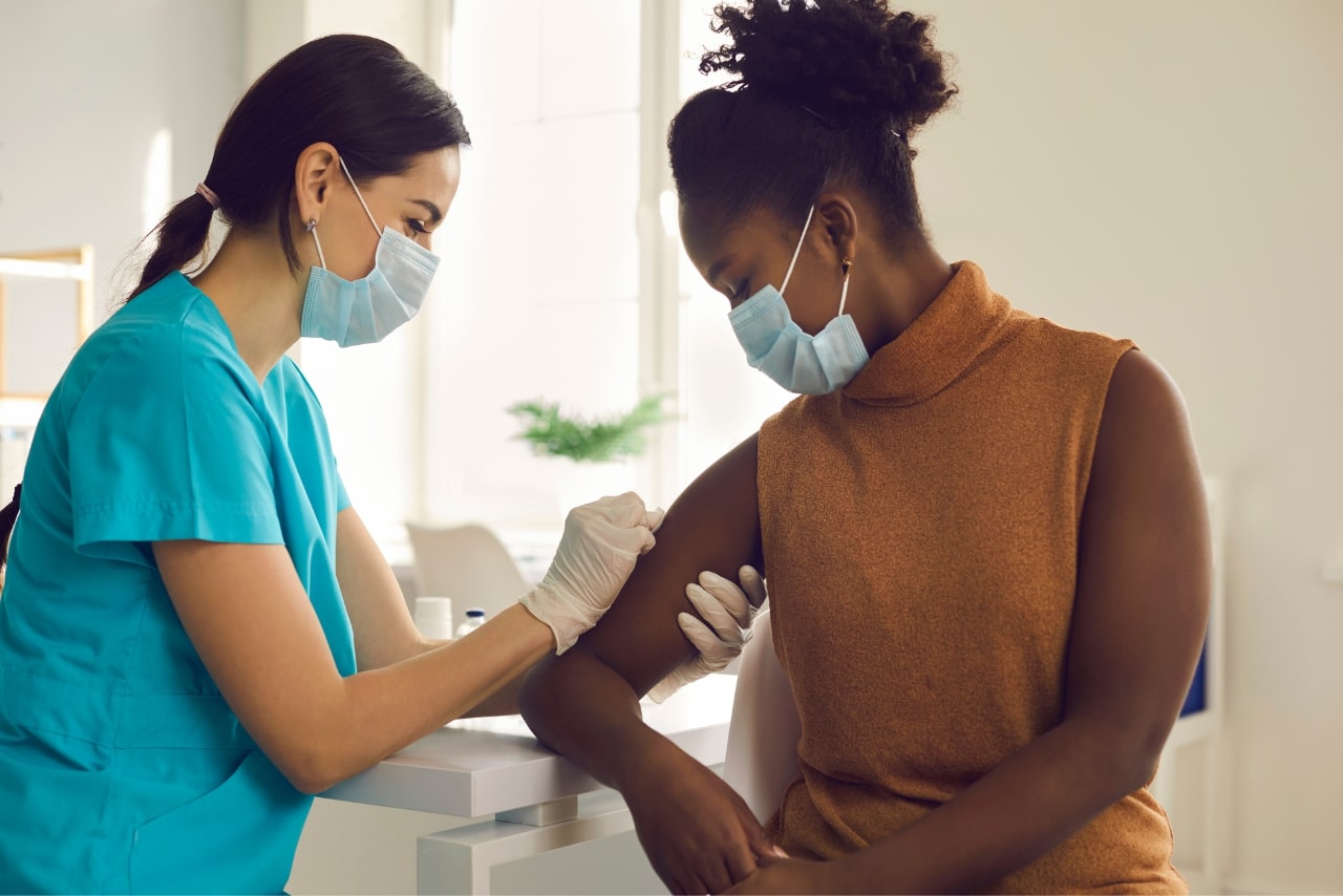 Nurse in medical masks while cleaning patient's arm while injecting.