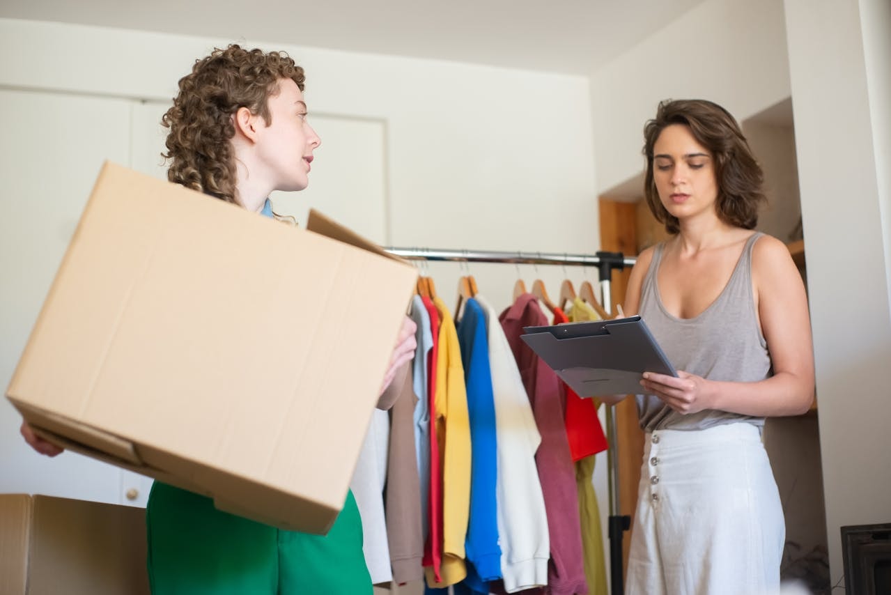 Two women discussing with one holding a shipping box and the other looking at a clipboard
