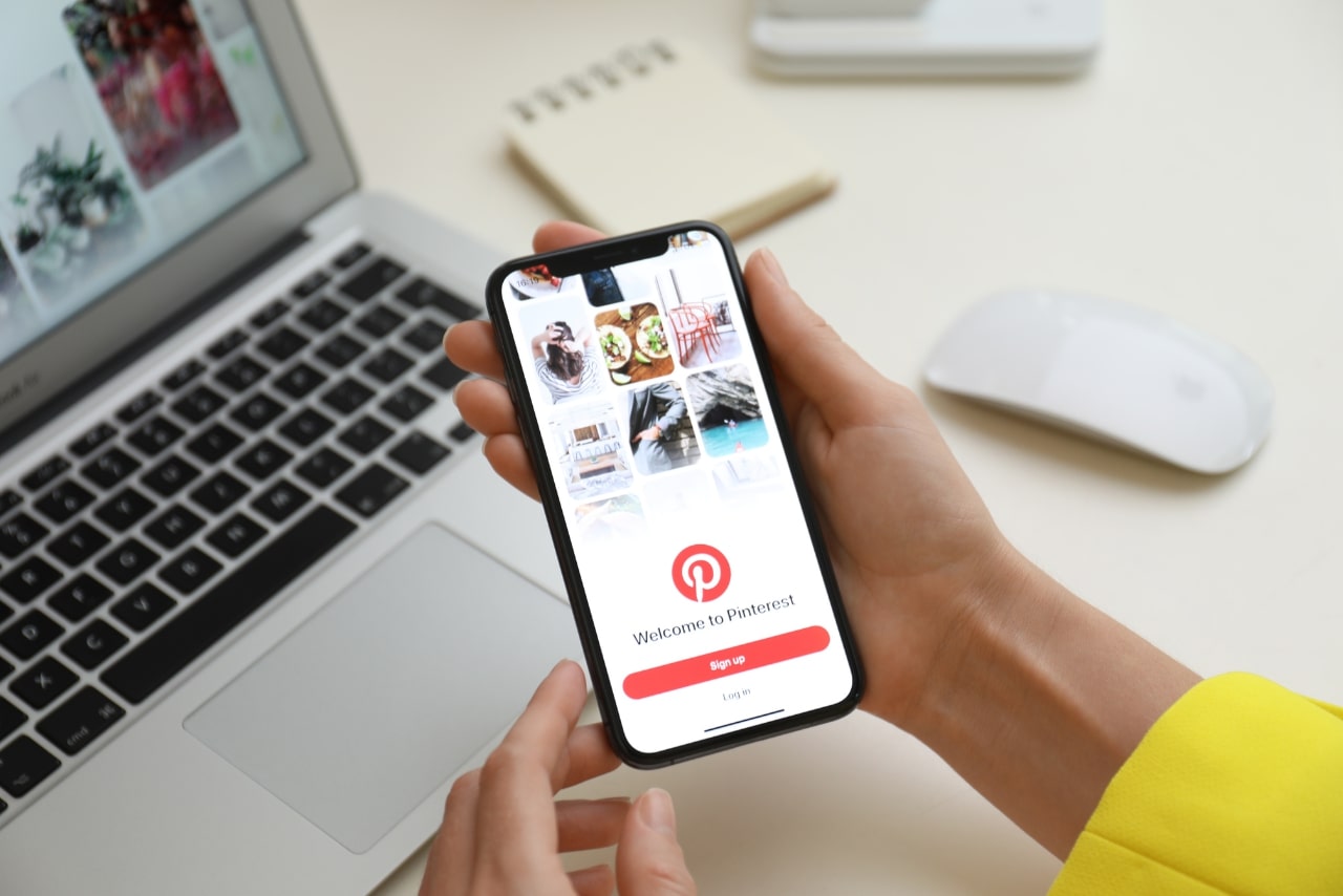 Woman Holding IPhone 11 with Pinterest App on Screen at Table.