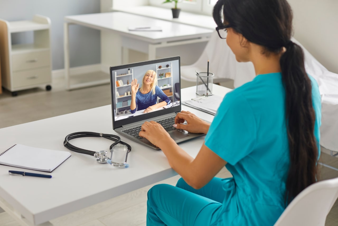 Woman nurse in blue uniform sitting at desk and working online on laptop in medical clinic.