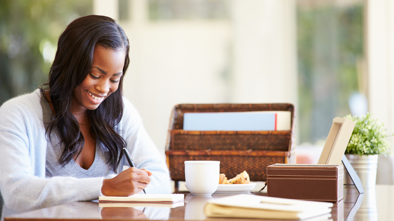 Woman writing on table sitting on desk.