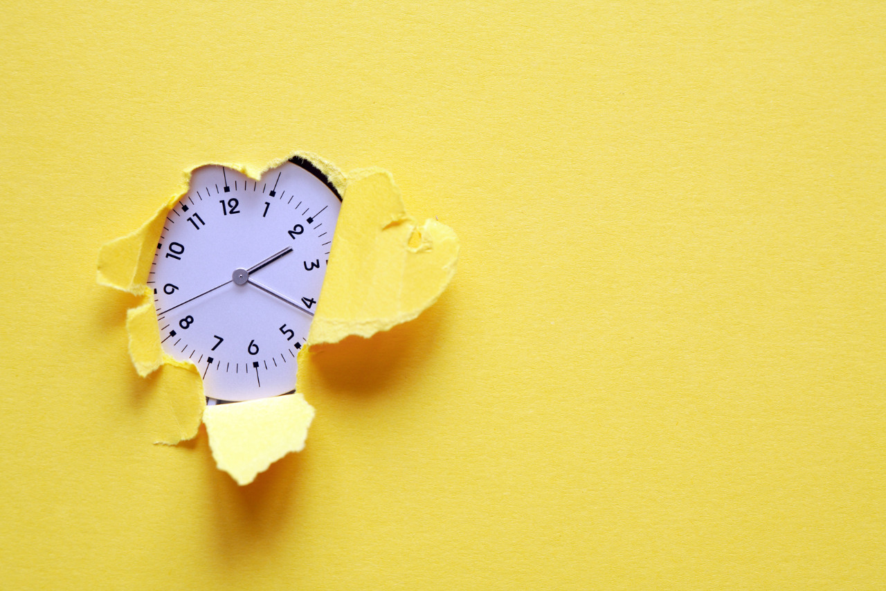 Clock inside whole in yellow paper sheet.