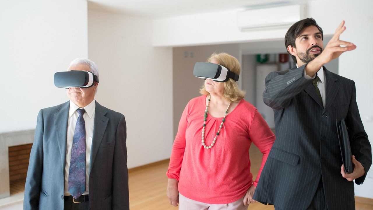 A Real Estate agent explaining things inside a rental unit to two seniors wearing VR goggles.