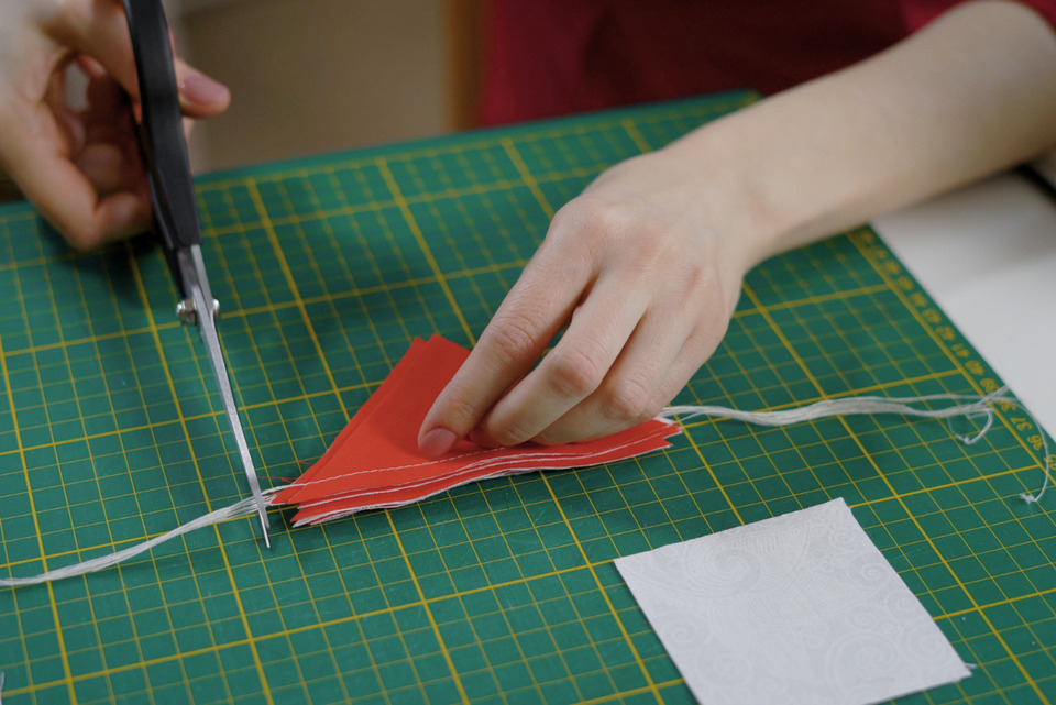Cutting piece of sweater into triangles with metal scissors.