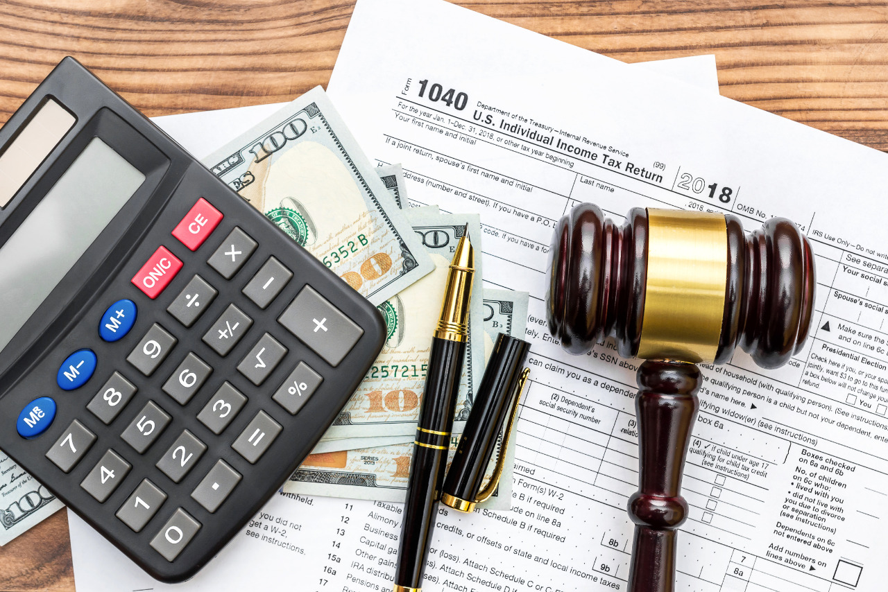 Calculator, gavel, pen, money and tax forms on table.