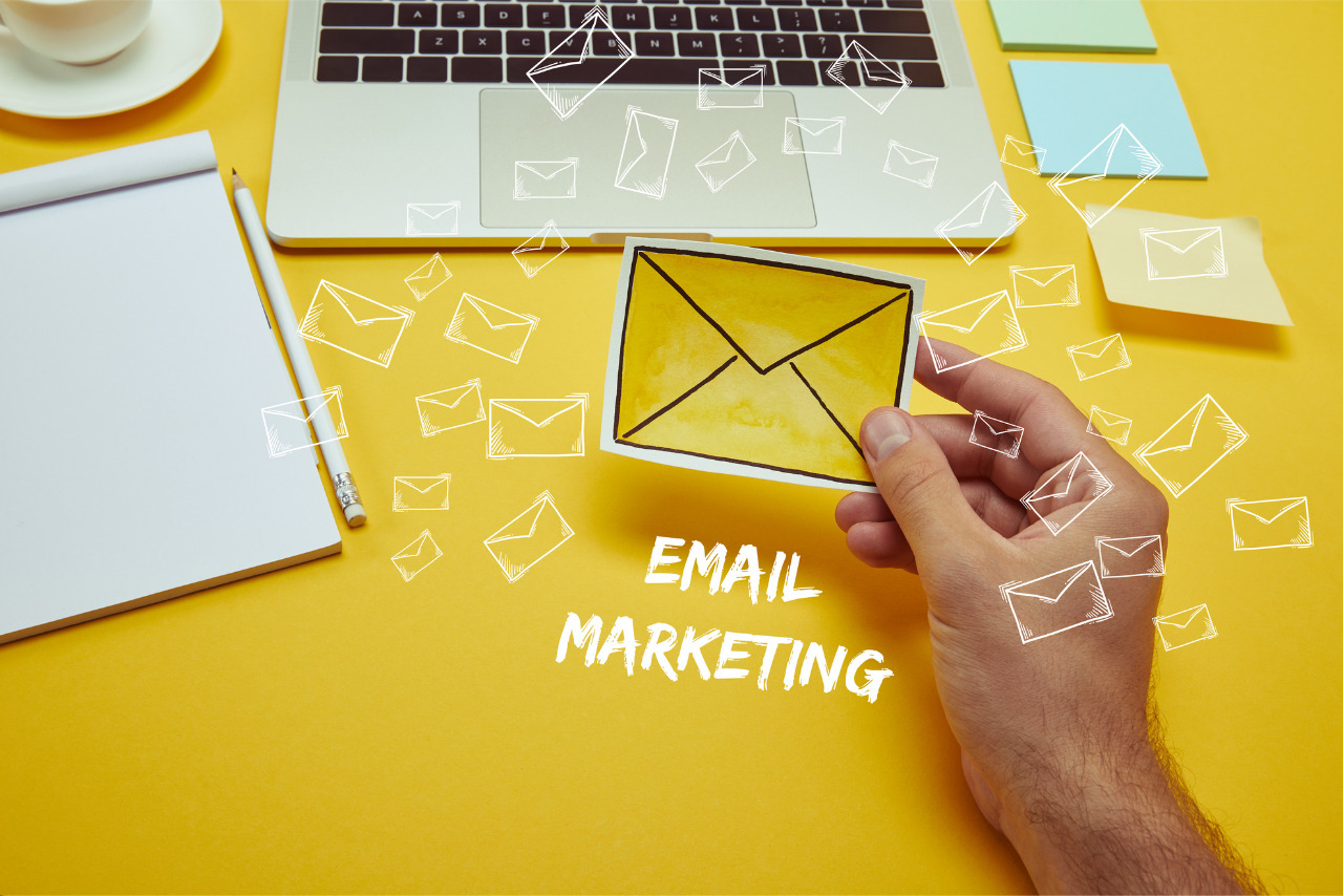 A hand holding a yellow paper envelope surrounded by floating envelope illustrations.