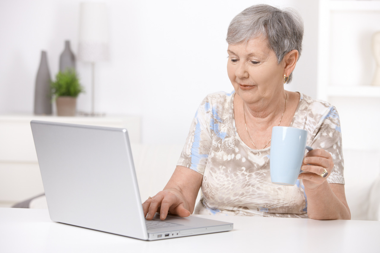 Senior woman does online shopping on laptop while holding mug.