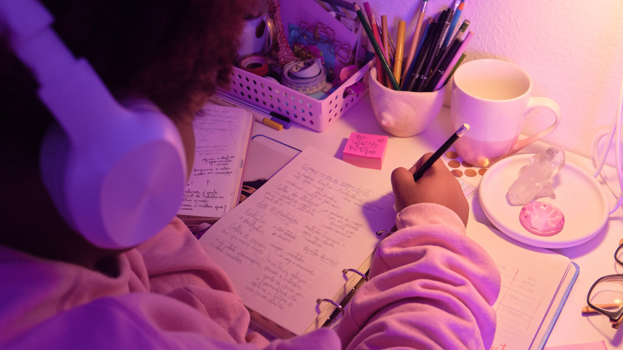 Woman's backview listening to podcast while jotting down.