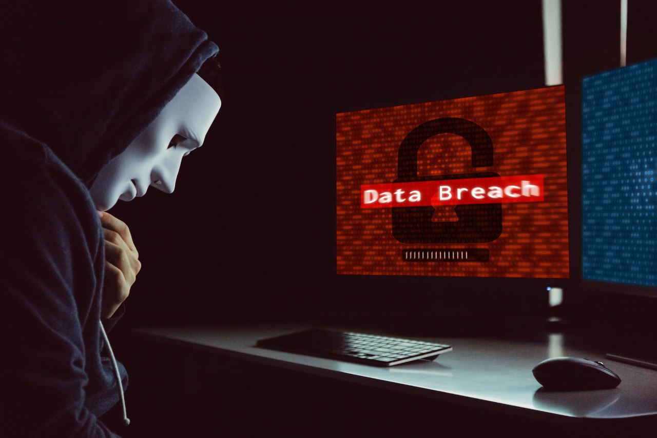 Masked hacker under hood using computer to commit data breach crime.