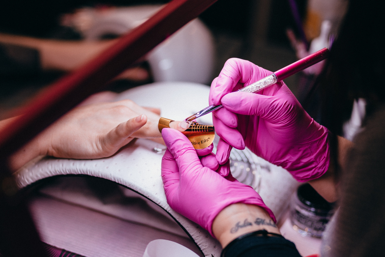 A woman receiving a manicure as a technician carefully applies nail polish.
