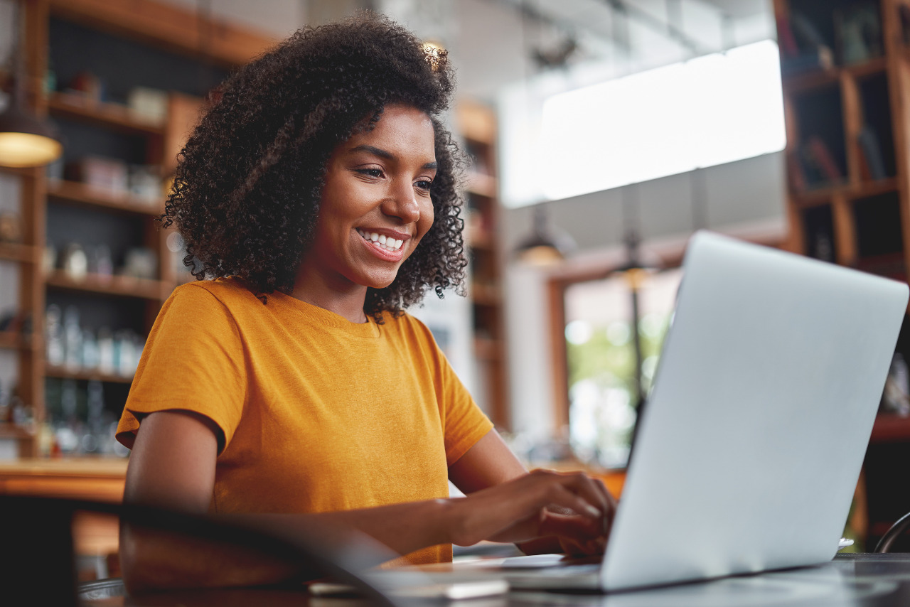 Happy young black woman using laptop in cafe.