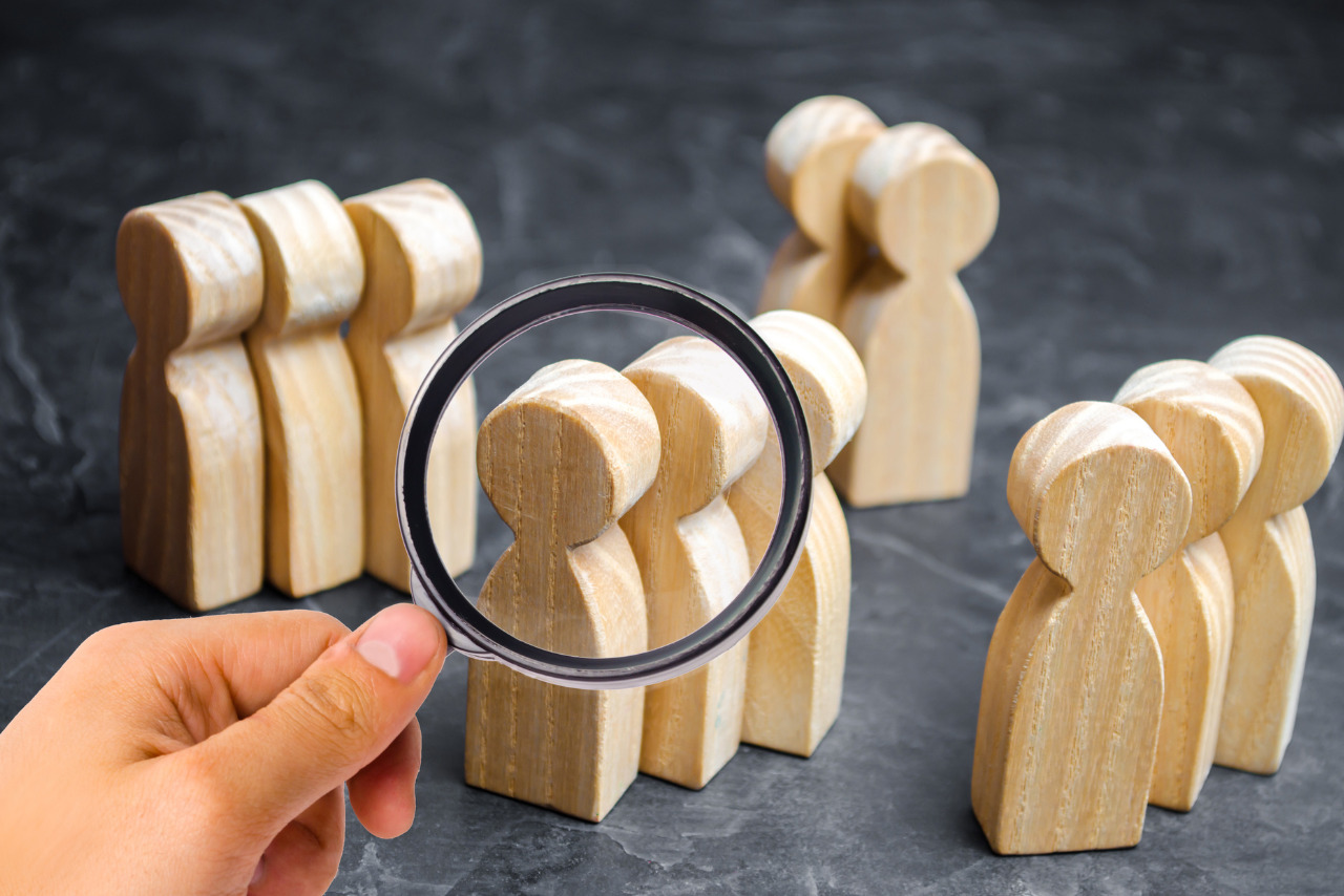 A hand holding a magnifying glass enlarges a group of wooden figurines.
