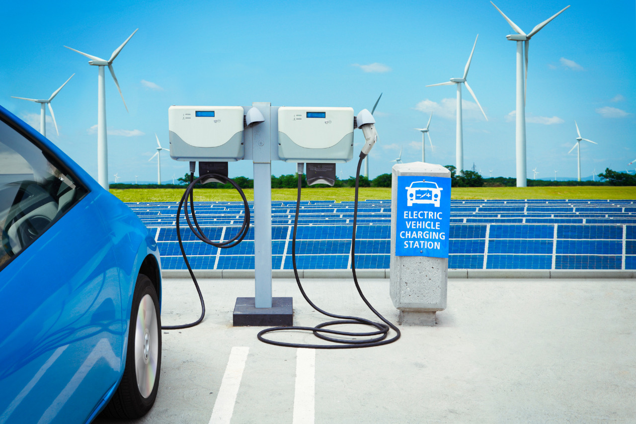 Car charging from an Electric vehicle charging station with windmills and solar panels at the back.