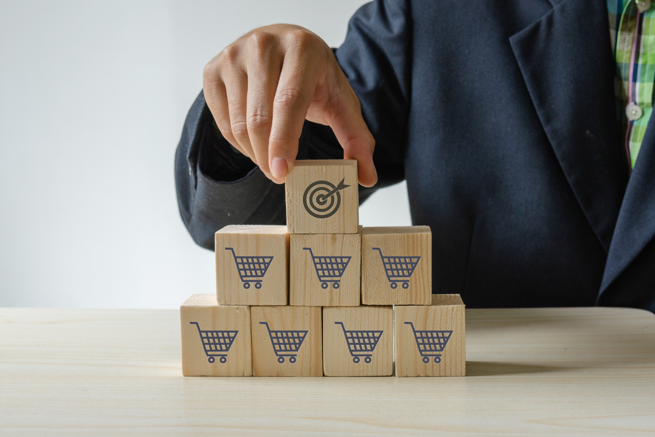 A hand placing a wooden block with a target icon on top of shopping cart blocks to indicate sales volume.