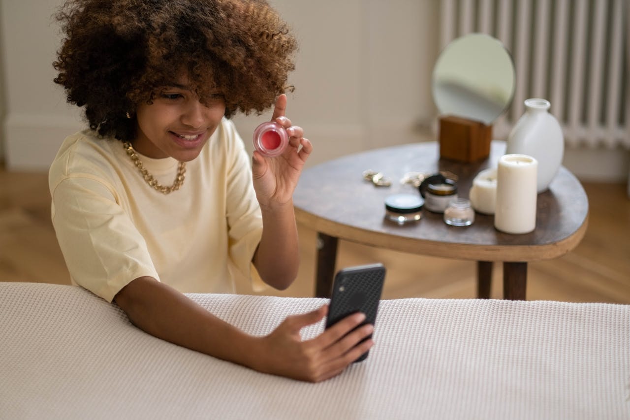 A woman holding a cosmetic product in front of a smartphone
