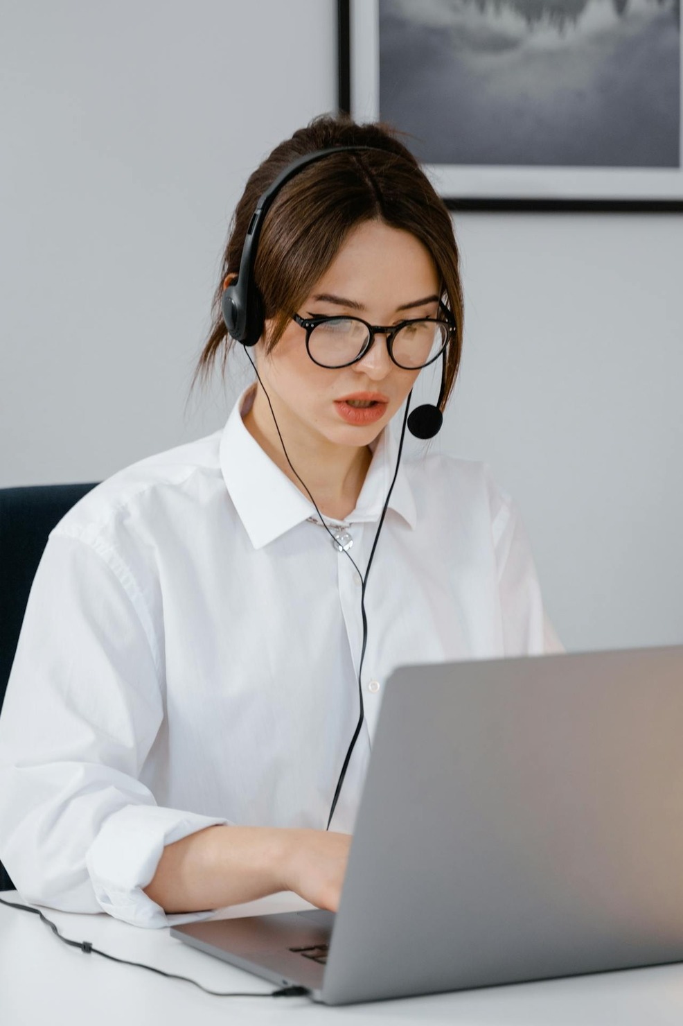 A woman talking on a headset while typing on her laptop