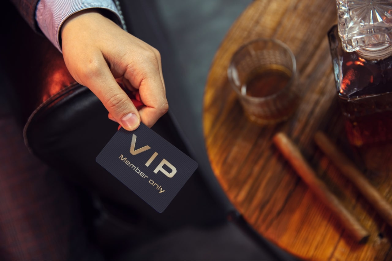 Gentleman's hand that holds exclusive VIP membership card next to the wooden table glass and cigars.