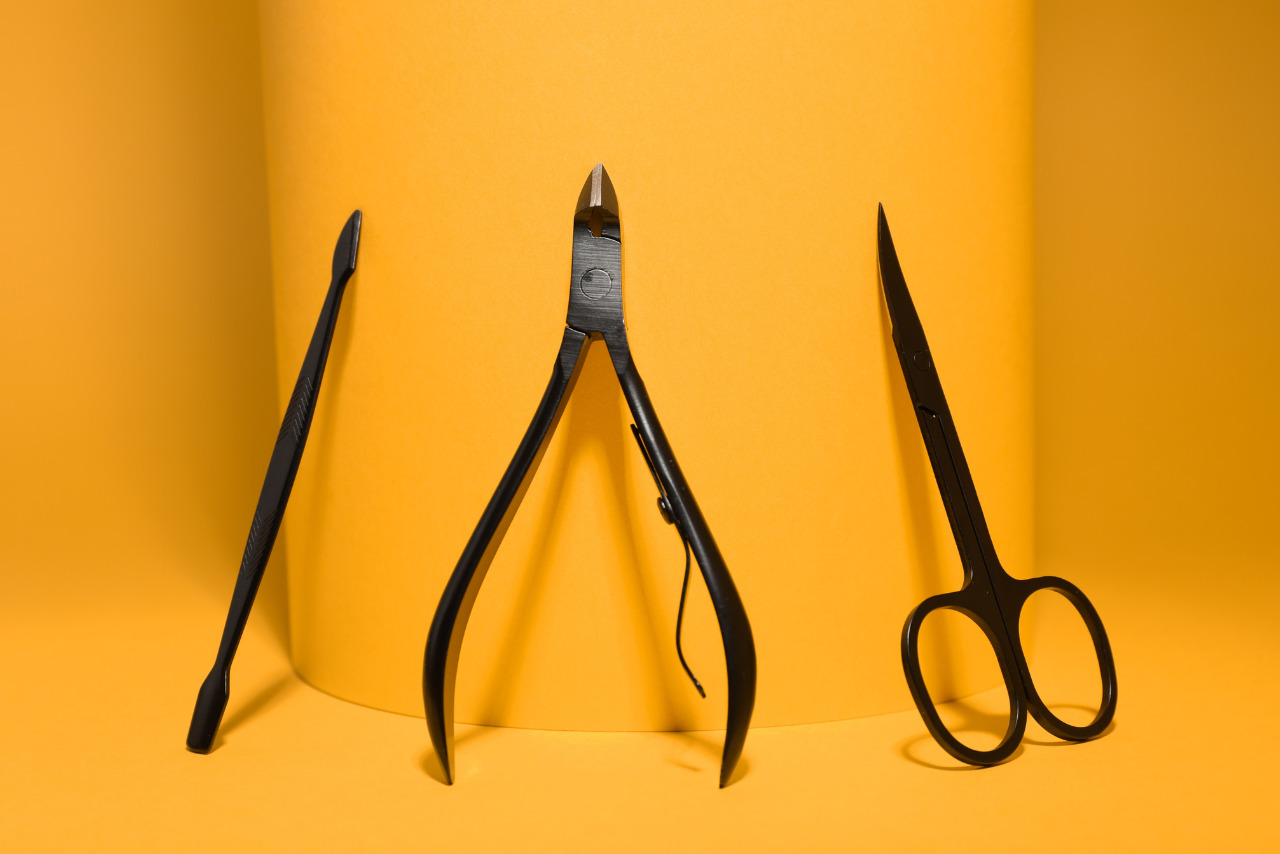 Manicure Scissors, Cuticle Nippers and Pusher on Yellow Background.