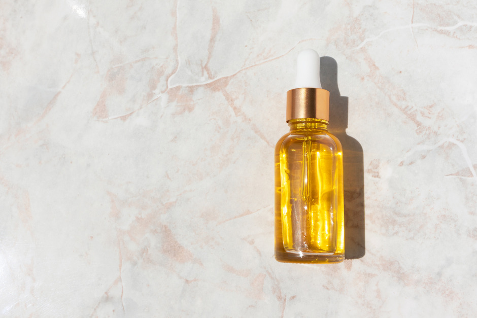 Oily serum in glass bottle with pipette on marble top.