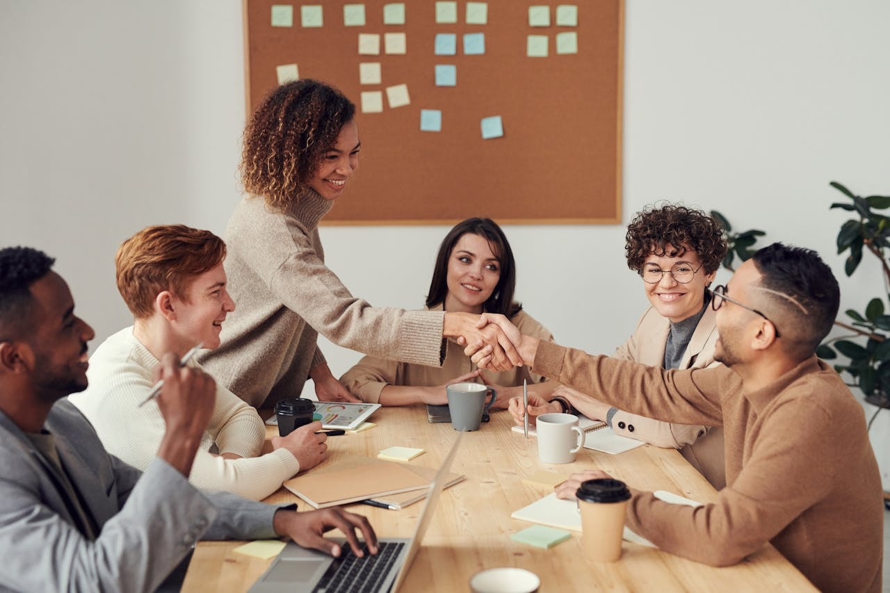 People in a meeting room with two colleagues shaking each other's hands