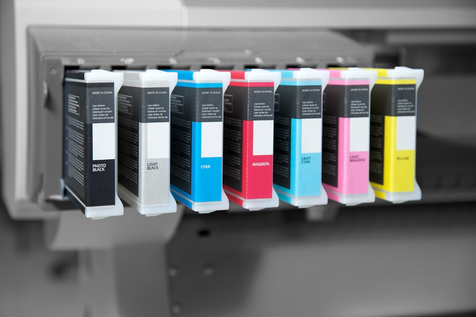 Row of ink cartridges in an office printer in CMYK colour palette.