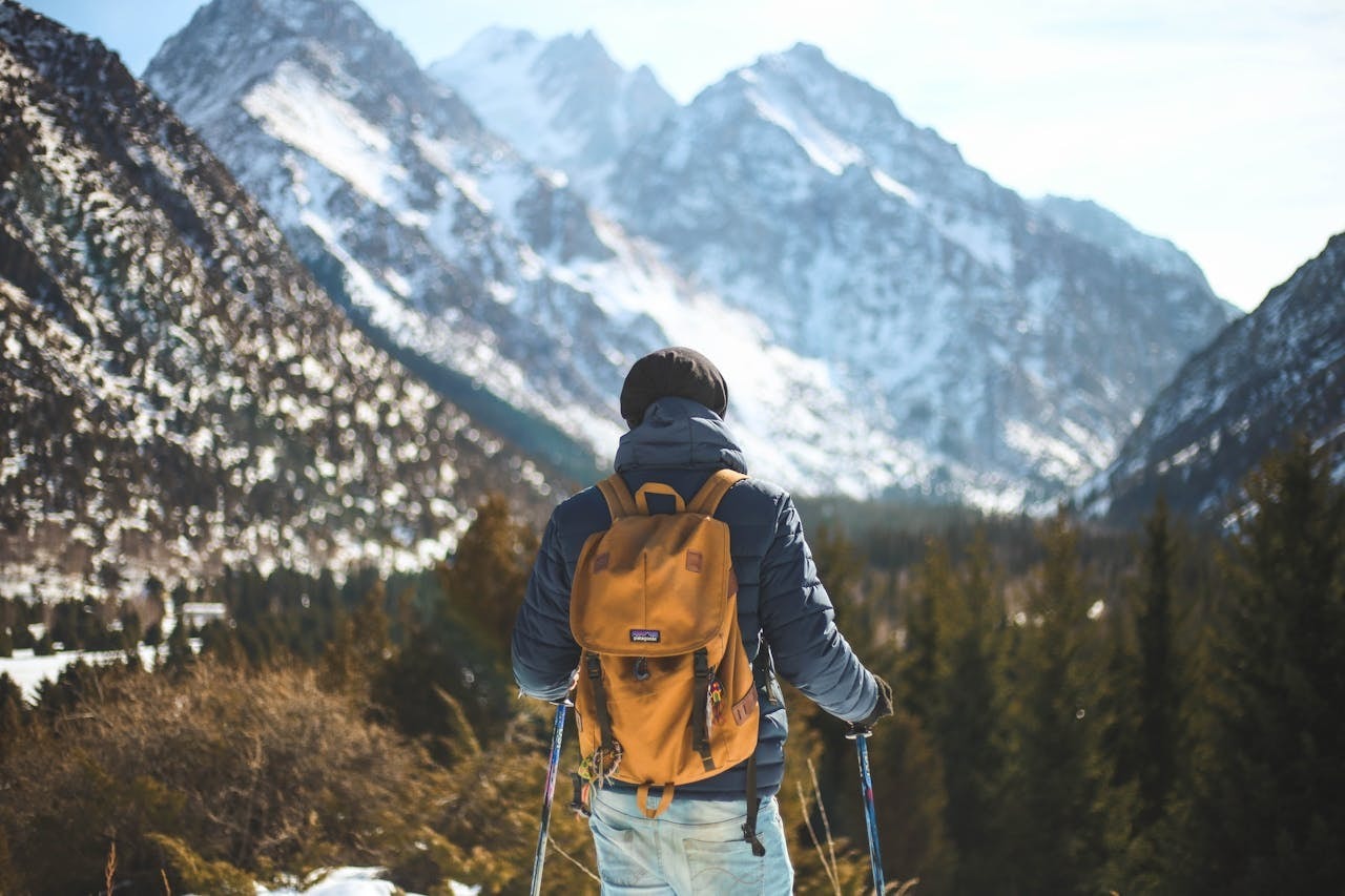A man wearing a blue jacket and brown backpack looking at a mountain