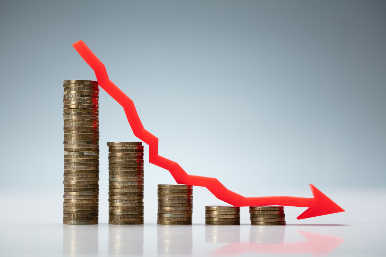 A graph with a downward arrow overlaying a stack of coins, symbolizing a decline in sales.