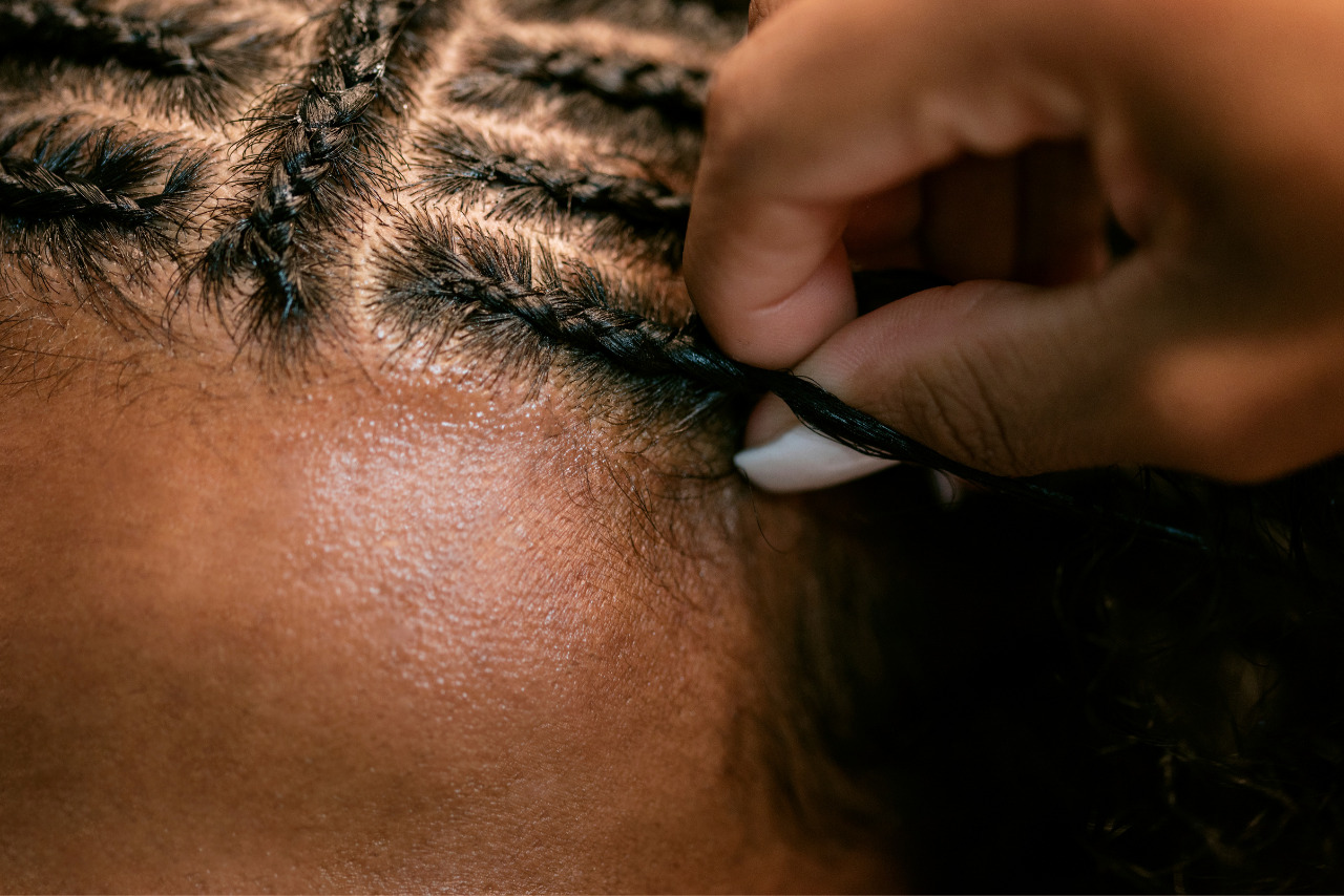 Close-up of man with curly hair getting braids.
