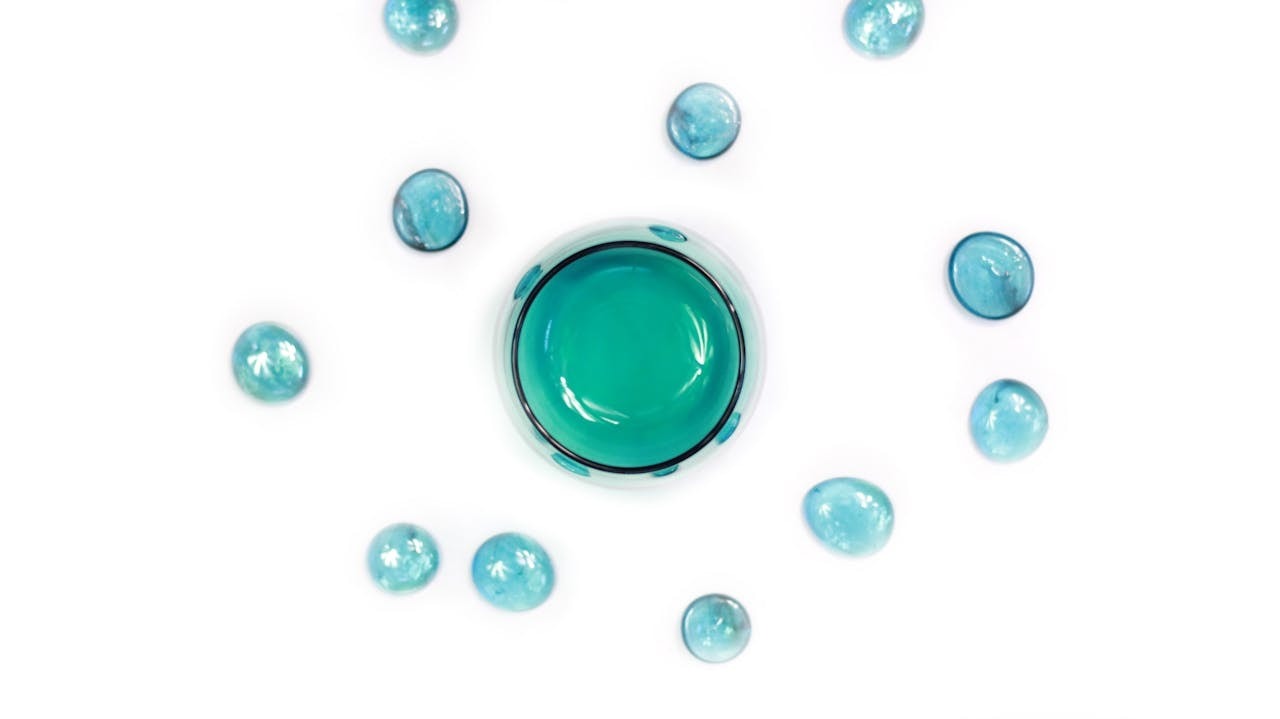 A photo of a blue bottle and droplets on a white background