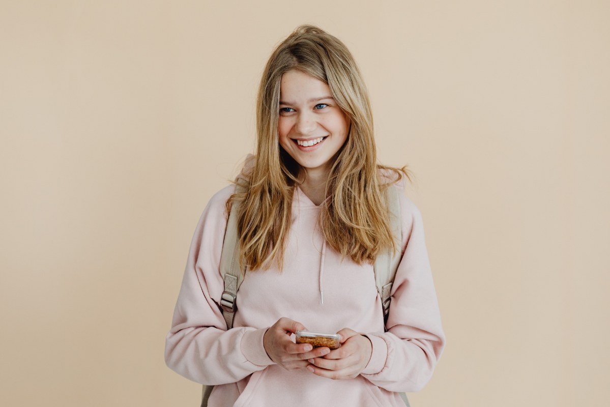 A 13-year old girl smiling and holding phone.