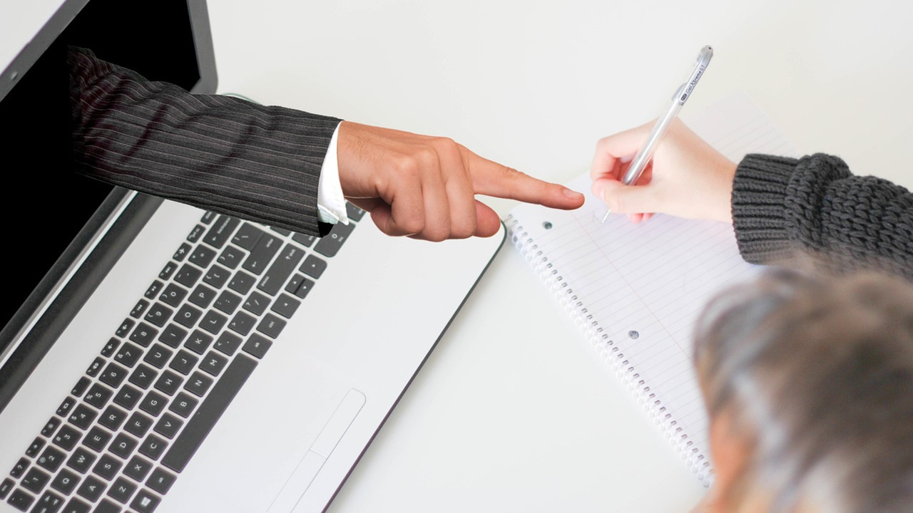A freelancer engaging in an online course: a guiding hand points toward them as they write diligently.