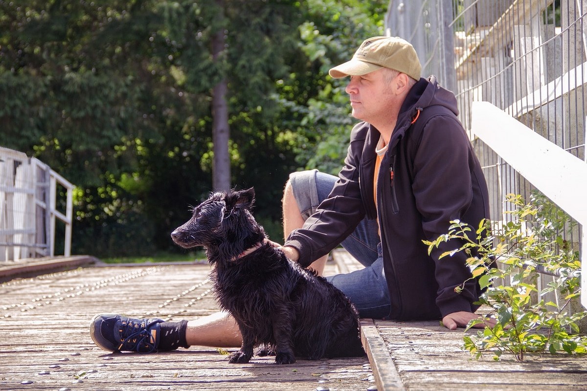 A man sitted next to a dog with wet fur.