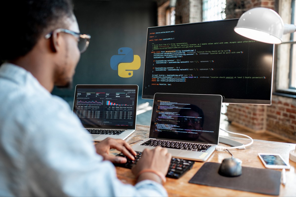 Behind view of man codes using multiple computers with python logo floating infront.
