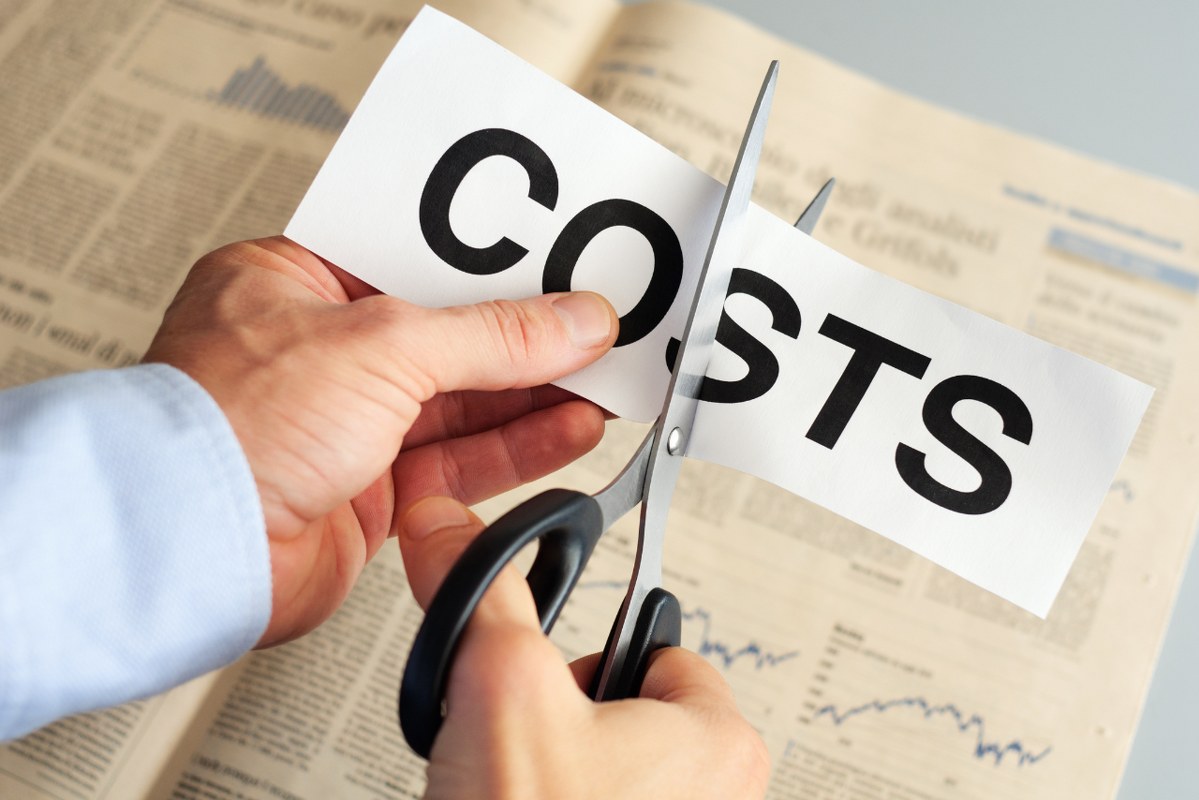 Business man's hands cutting paper with Costs written on it.