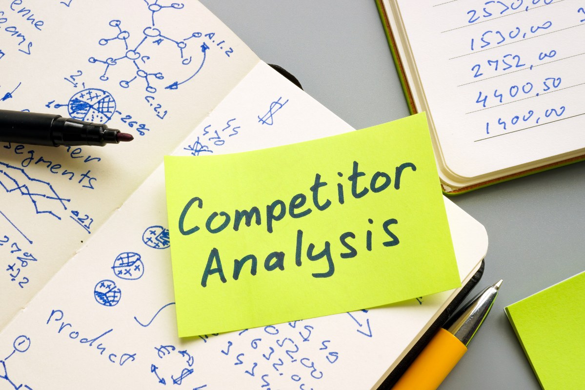 Competitor Analysis on yellow sticky note on top of notebooks.