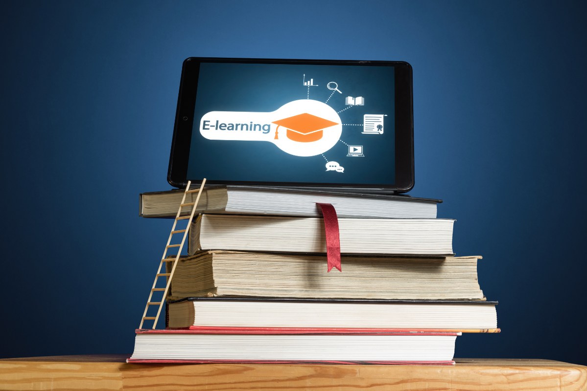 E-learning text with graduation hat on tablet screen while sitting on top of several books.