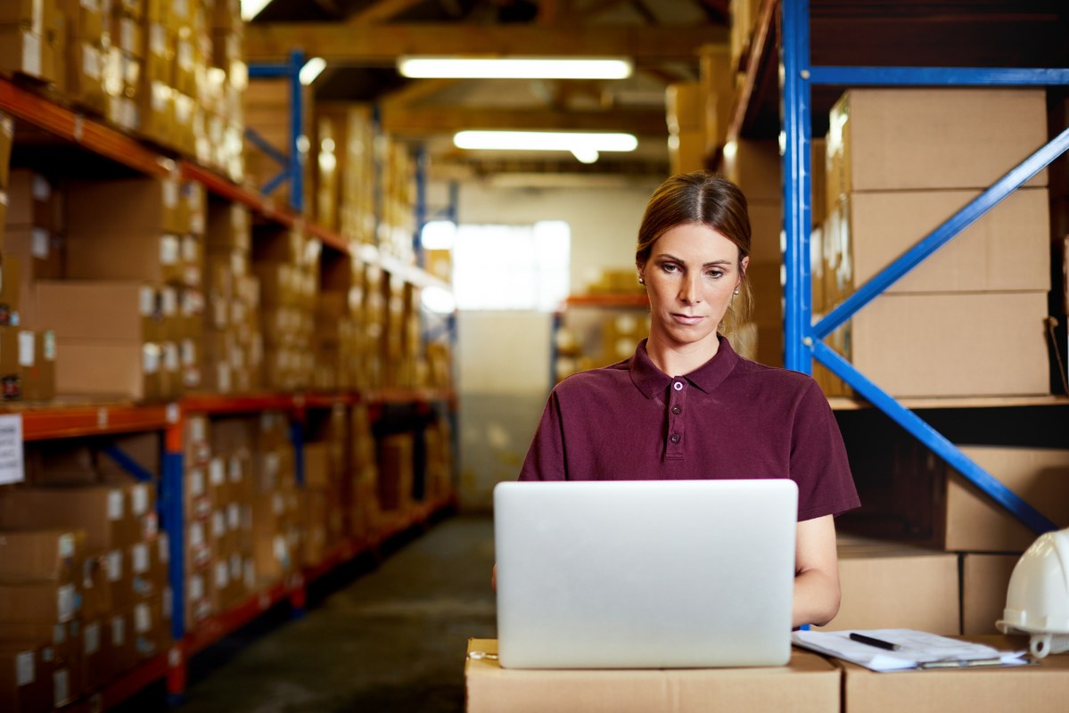 Female supplier works on laptop while at warehouse.