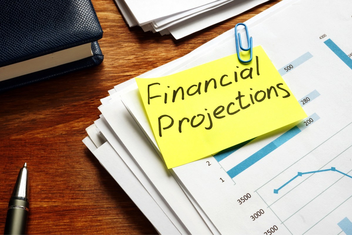 Financial Projections on yellow sticky note paperclipped on stack of data papers.
