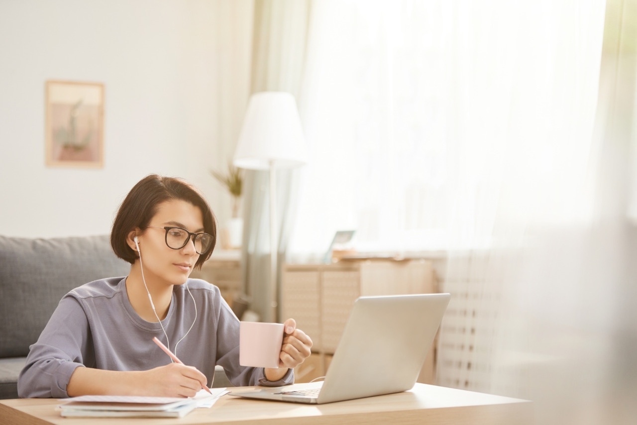 Focused freelancer in glasses, drinking coffee and transcribing audio at a cozy apartment table.