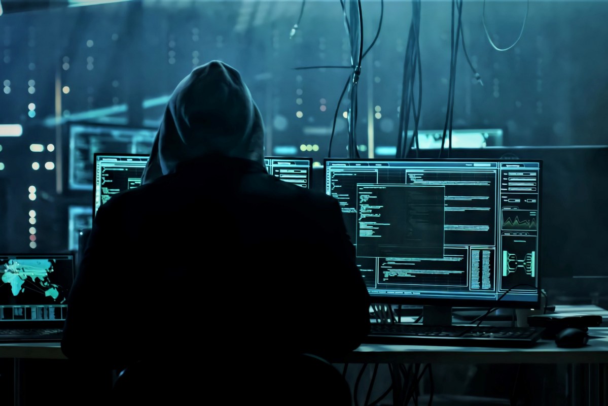 Hacker's backview working on multiple laptops.