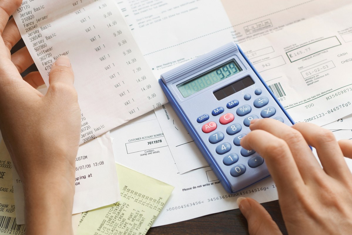 Hand holds receipt representing expenses then the other hand uses calculator.