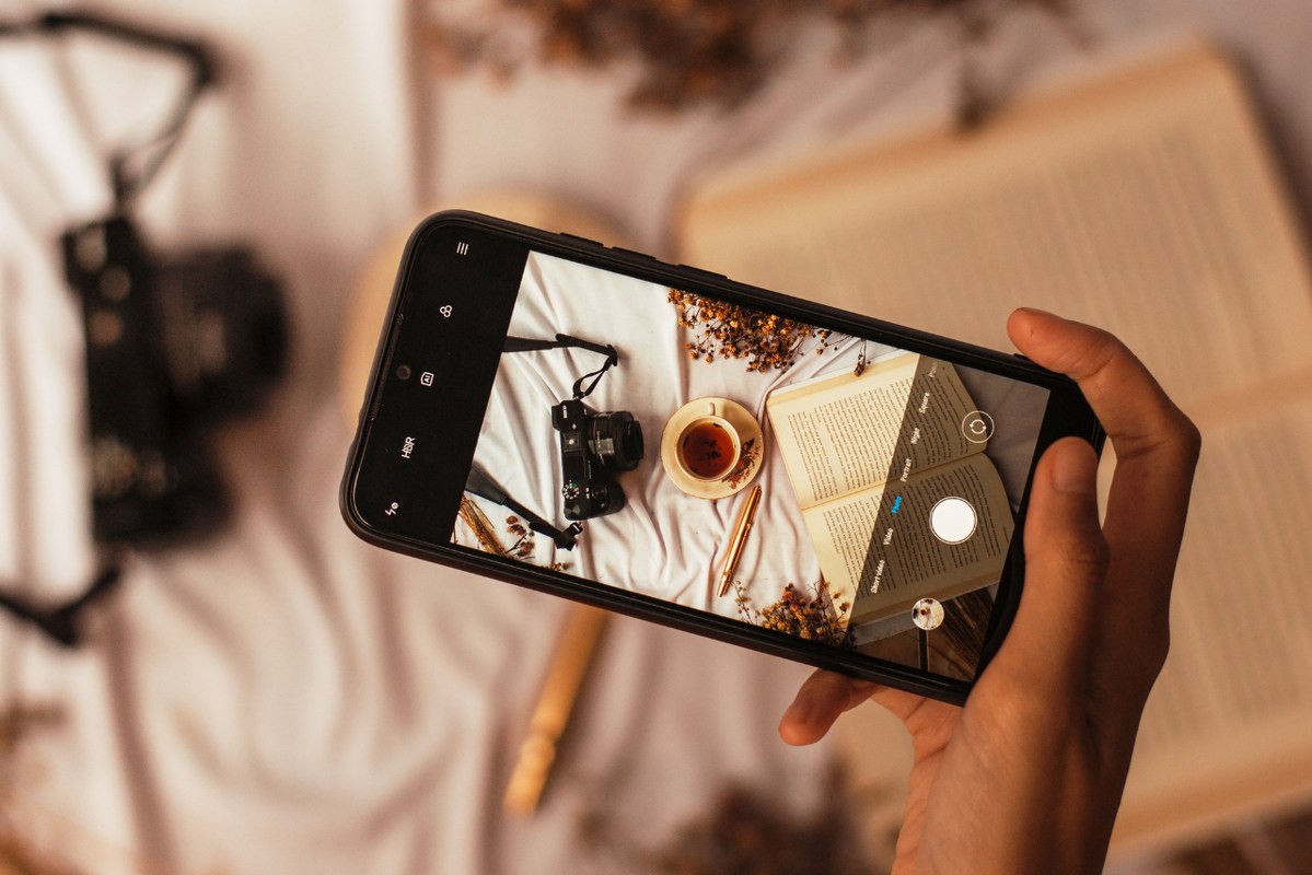 Hand takes clear photo of cup and book using phone.