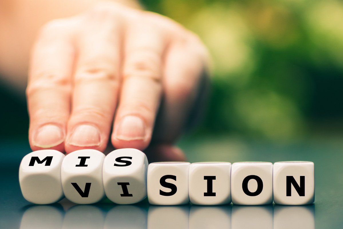 Hand turns dice and changes the word vision to mission.