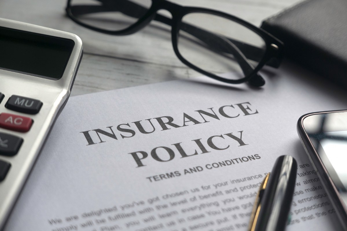 Insurance document on table with glasses, pen and calculator.